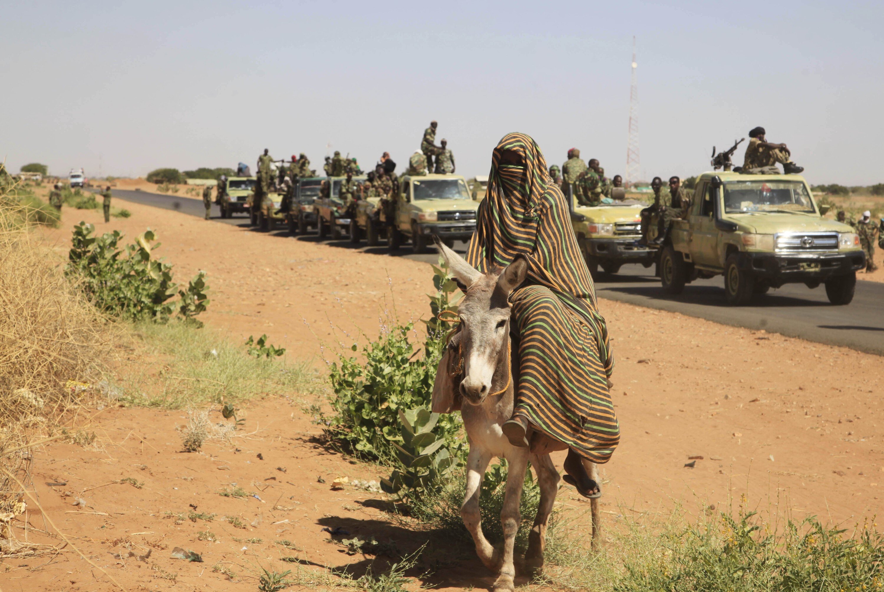 FILE - In this Nov. 20, 2014 file photo taken on a government organized media tour, a woman rides a donkey past a convoy of government troops in Tabit village in the North Darfur region of Sudan, where allegations surfaced of rape of women by government allied troops. In January 2019, Al-Bashir is facing a tough challenge to his grip on power as street protests show no sign of abating. In the 2000s, Sudan was most known for the brutal repression of an uprising in its western Darfur region, when the pro-government militias known as the Janjaweed became notorious for atrocities and al-Bashir himself was indicted by the International Criminal Court for alleged war crimes and genocide. (AP Photo/Abd Raouf, File)