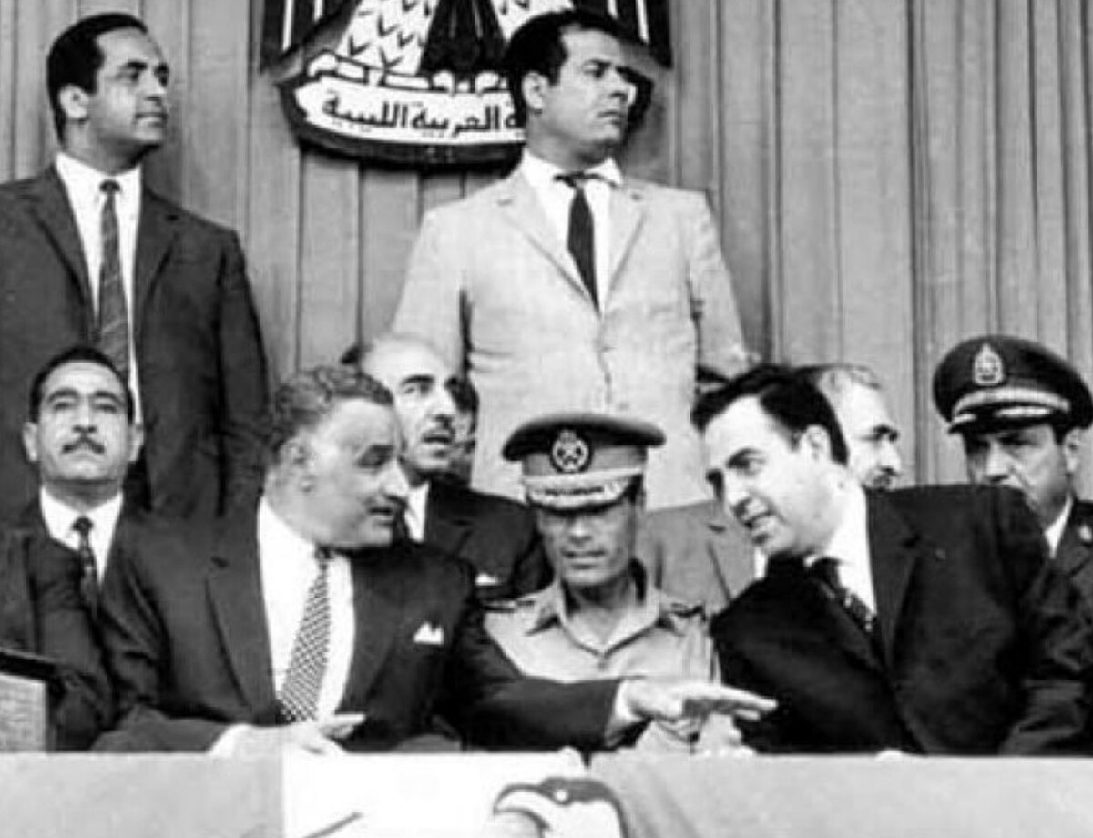 Gaddafi at an Arab summit in Libya shortly after the September Revolution that overthrew King Idris. Gaddafi, in military uniform, sits in the center between Egyptian President Gamal Abdel Nasser on the left and Syrian President Nureddin al-Atassi on the right