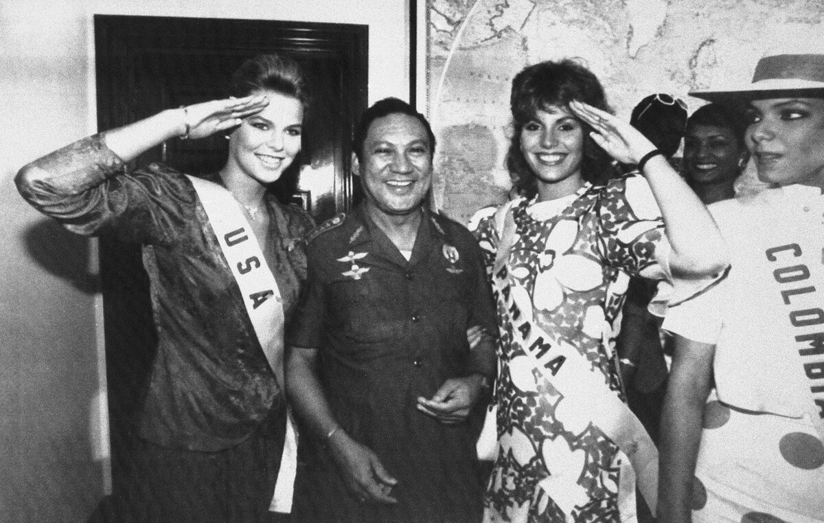 Na ovoj fotografiji od 5. srpnja 1986. Miss SAD-a, Christy Fichtner, lijevo, i Miss Paname, Gilda Garcia Lopez, pozdravljaju dok stoje uz generala Manuela Antonia Noriegu u Panama Cityju. Na slici desno je Miss Kolumbije, Maria Monica Urbina.