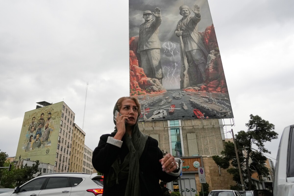 A woman talks on her cellphone as she walks past a billboard showing Rais Ali Delvari, a national hero in an early 1900 uprising against British forces in southern Iran in the Persian Gulf, right, and the late Revolutionary Guard's navy chief Alireza Tangsiri, who was killed in the U.S.-Israeli strike in late March 2026, commanding the closure of the Strait of Hormuz, on a building at a square in downtown Tehran, Iran, Monday, April 20, 2026. (AP Photo/Vahid Salemi)