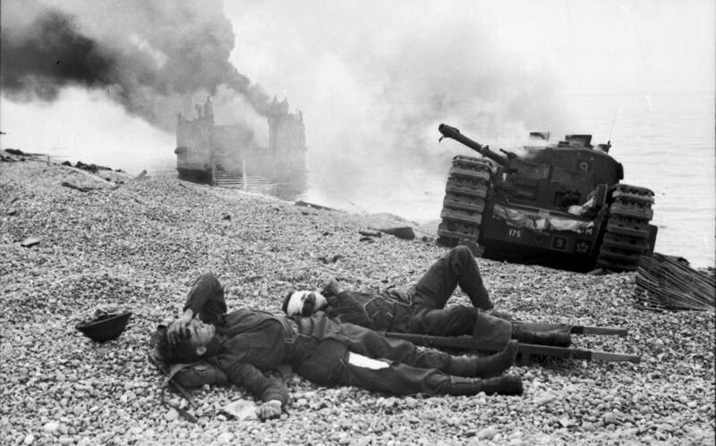 A wounded Canadian soldier and abandoned Churchill tanks after the raid. A landing craft burns in the background.