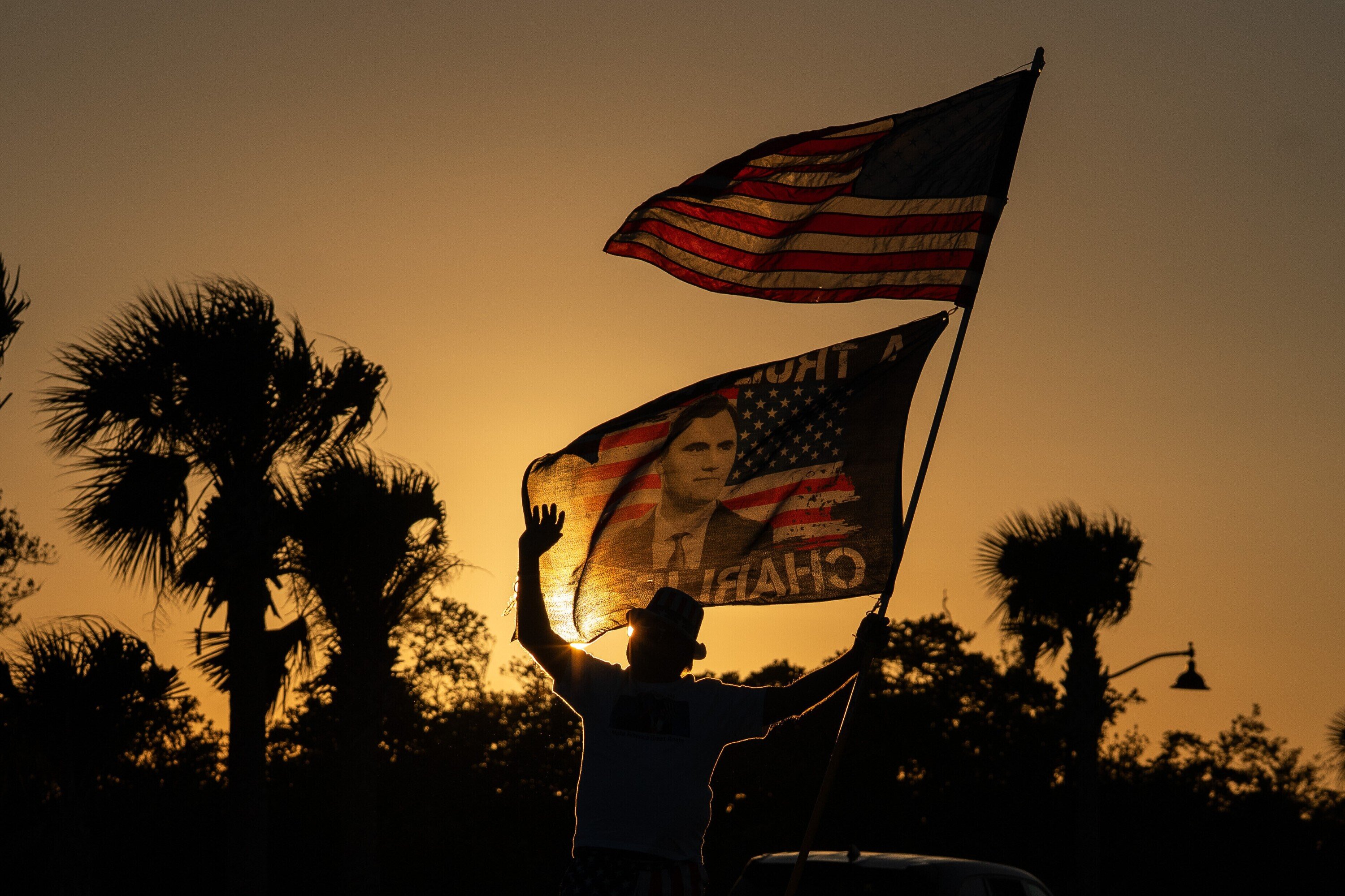 FILE - President Trump supporter Steve Emery holds a flag paying tribute to right-wing political activist Charlie Kirk along a bridge to Mar-A-Lago before President Donald Trump departs West Palm Beach, Fla., for Washington, Sunday, Jan. 4, 2026. (AP Photo/Allison Robbert, File)